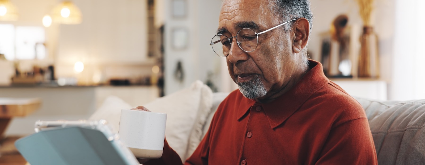 a man looking at an iPad and holding a cup